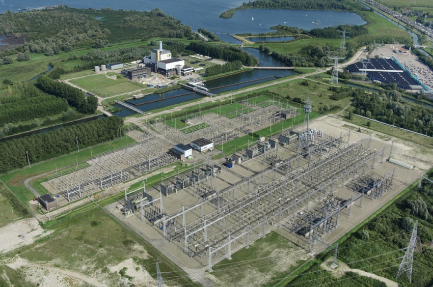 Luchtfoto van het nieuwe 380/150/20 kV-hoogspanningsstation bij Moerdijk, met portalen, transformatoren en hoogspanningslijnen naast een kanaal en industrieterrein.